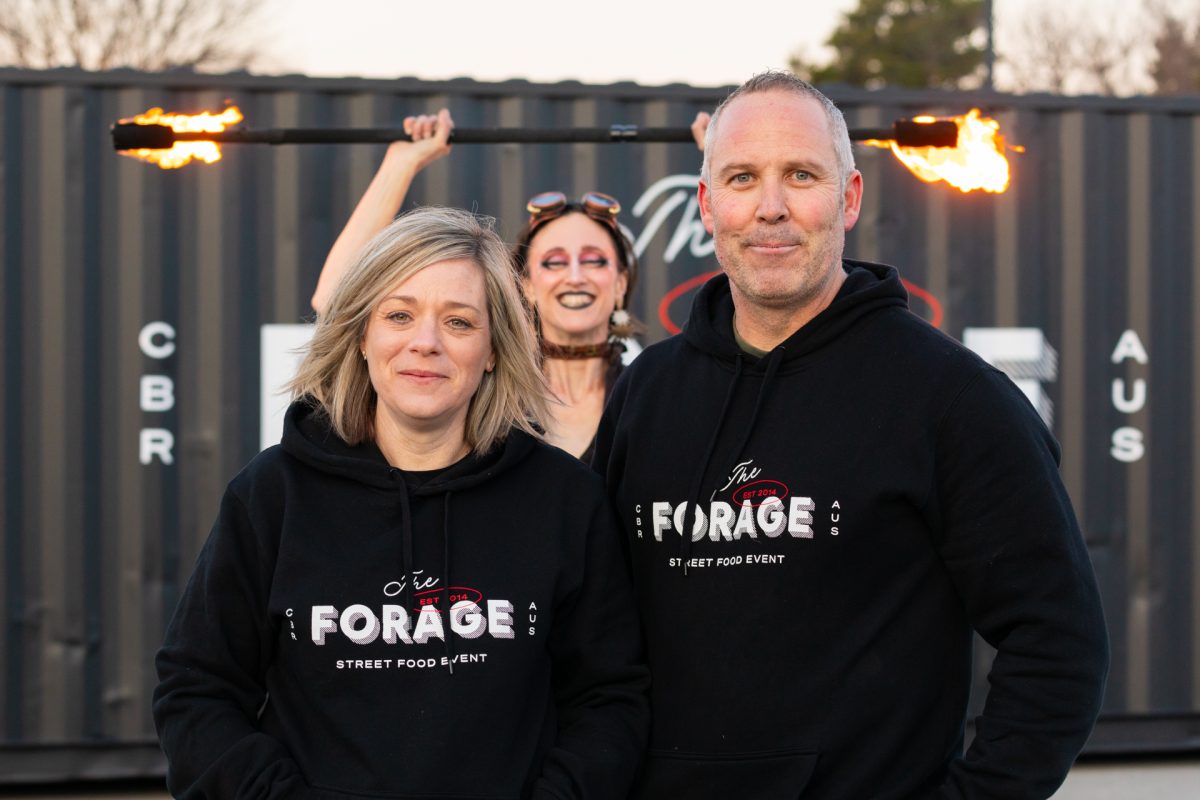 Two people in Forage branded jumpers with a fire twirler in the background.