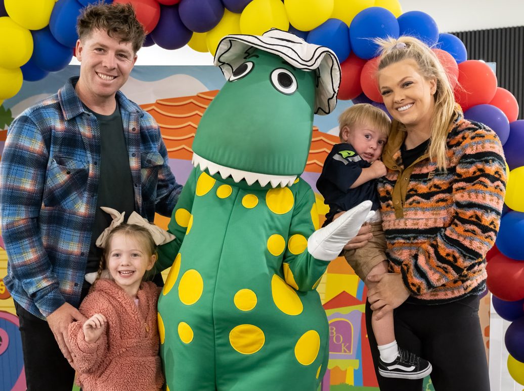 Family standing in front of balloons with a dinosaur costume character