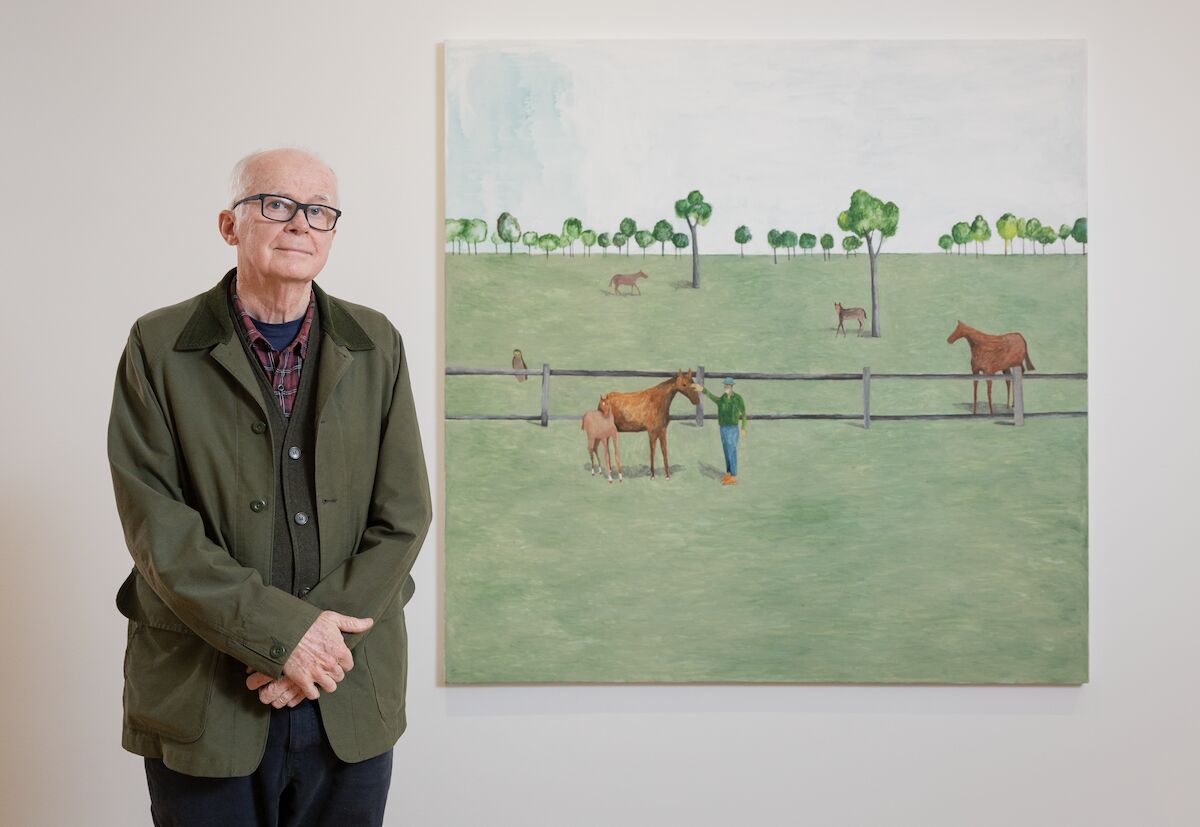 Man stands next to an artwork of horses in a paddock