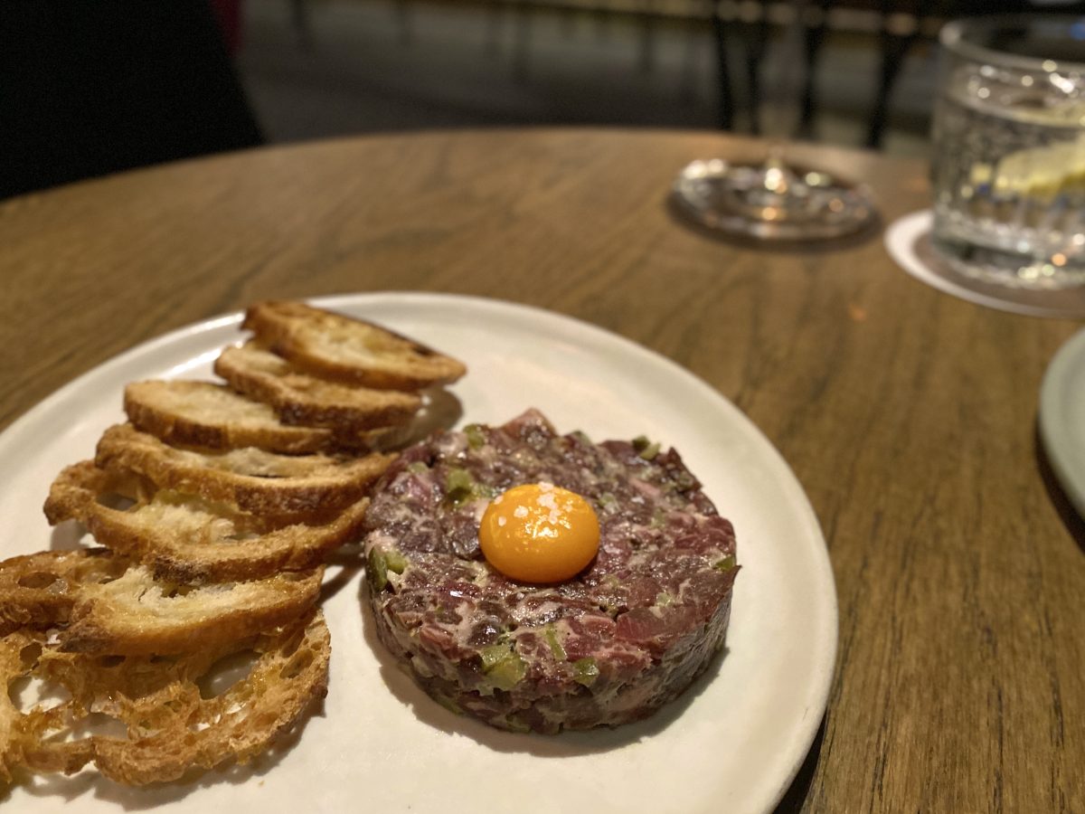 Plate of classic beef tartare, topped with a small egg yolk.