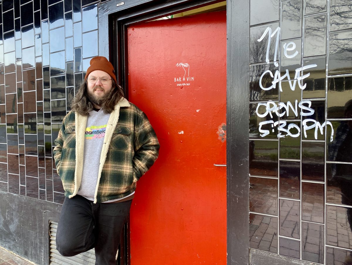 Brett stands next to the red door. 