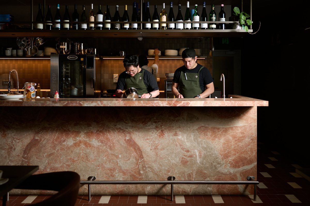 Chefs at work behind a pink marble counter.