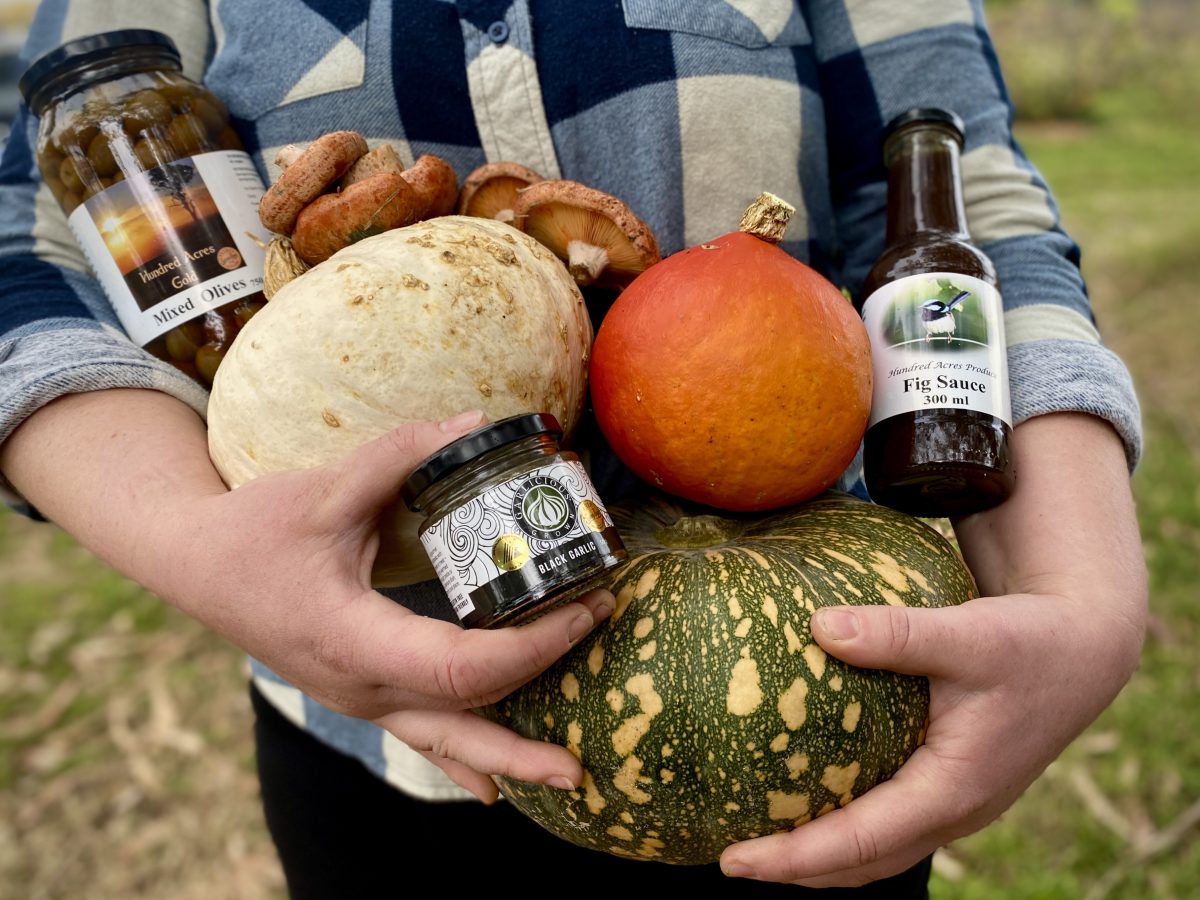 Hands holding a collection of colourful pumpkins, jars of olives.