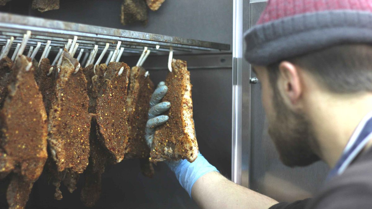 A worker inspects strips of seasoned meat hanging from hooks.