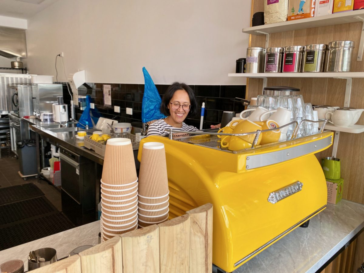 Christina makes a coffee using a bright yellow coffee machine.