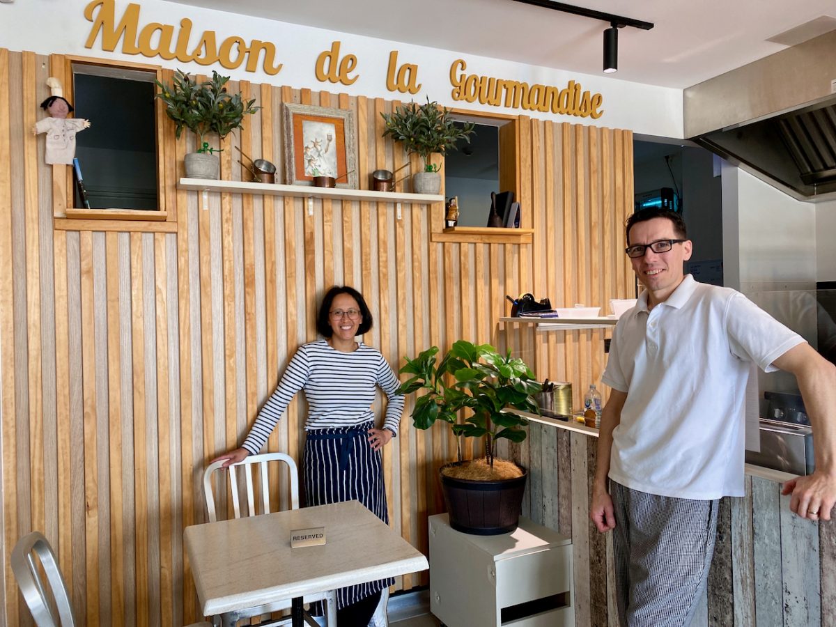 Thomas and Christina pose in front of a sign which reads 'Maison de la Gourmandise'