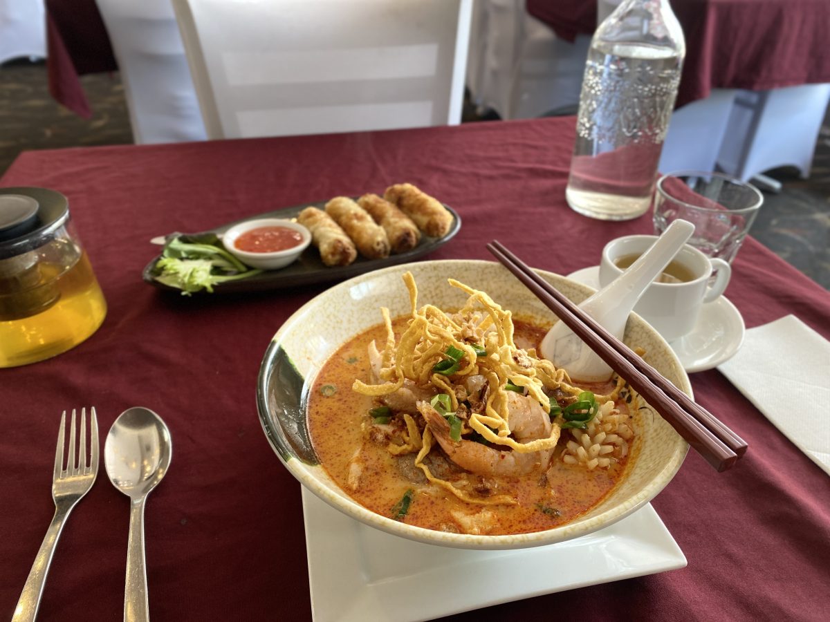 Bowl of laksa with dried noodles on top and a dish of spring rolls