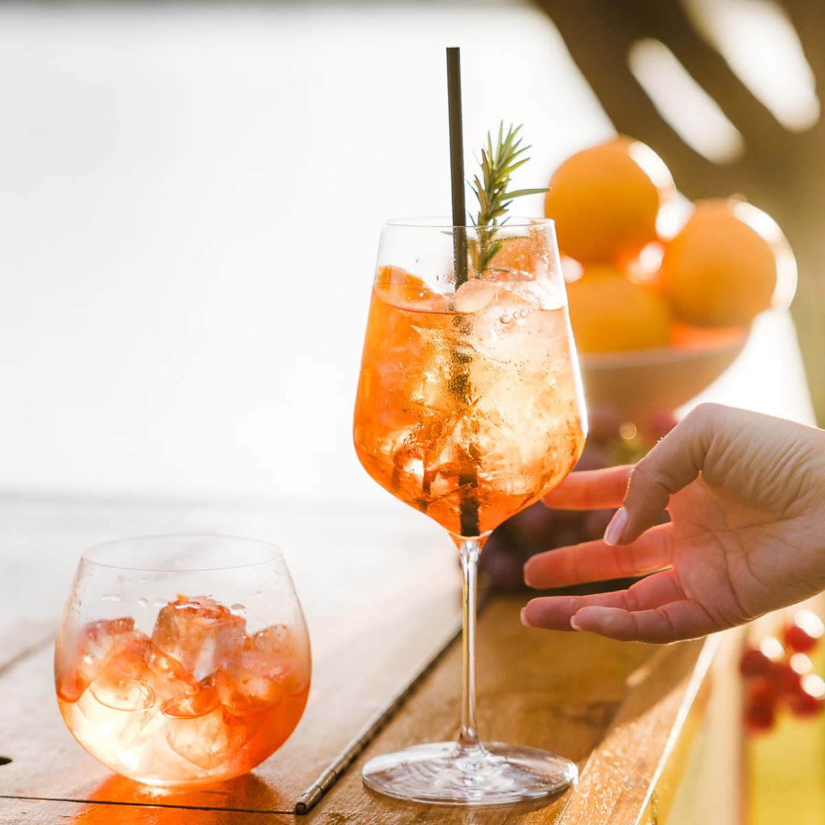 A hand reaching to pick up an orange cocktail in a wine glass.