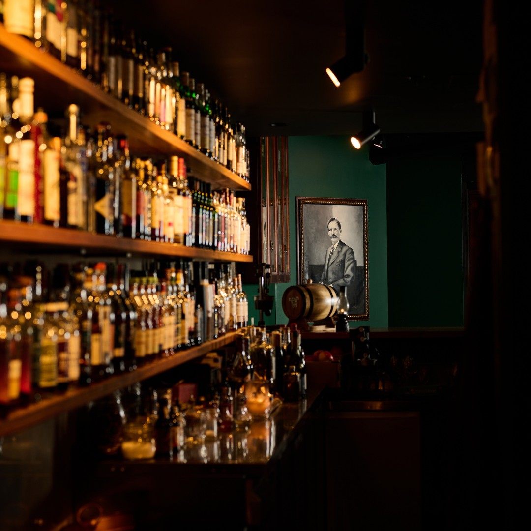 Interior of green-walled bar with many whisky bottles and a black and white vintage portrait.