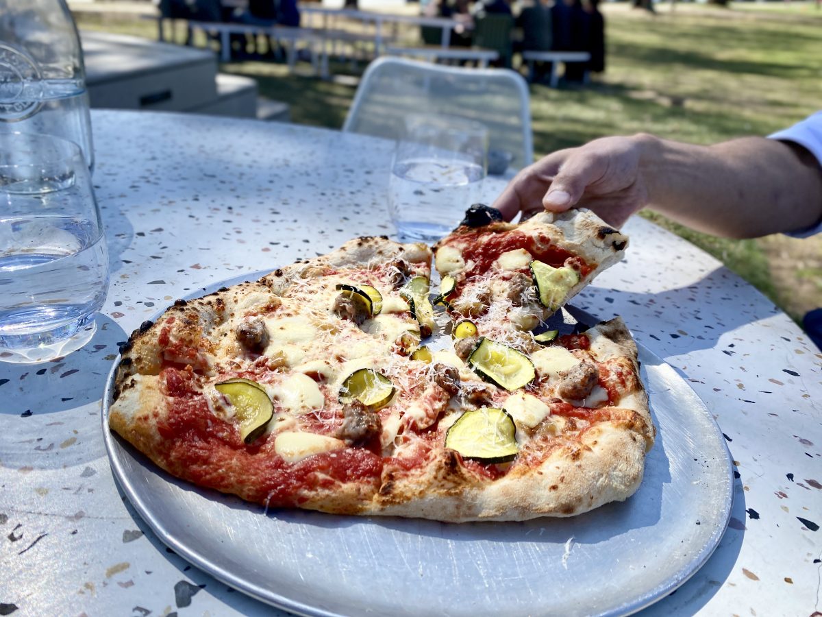 A hand picks up a piece of pizza on a terrazzo-patterned table.