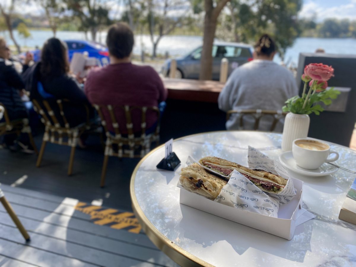 A large sandwich on a sun dappled table looking out over a lake.