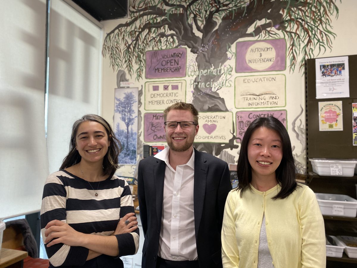 Three people stand at shop counter in front of a mural depicting the co-operative's values.