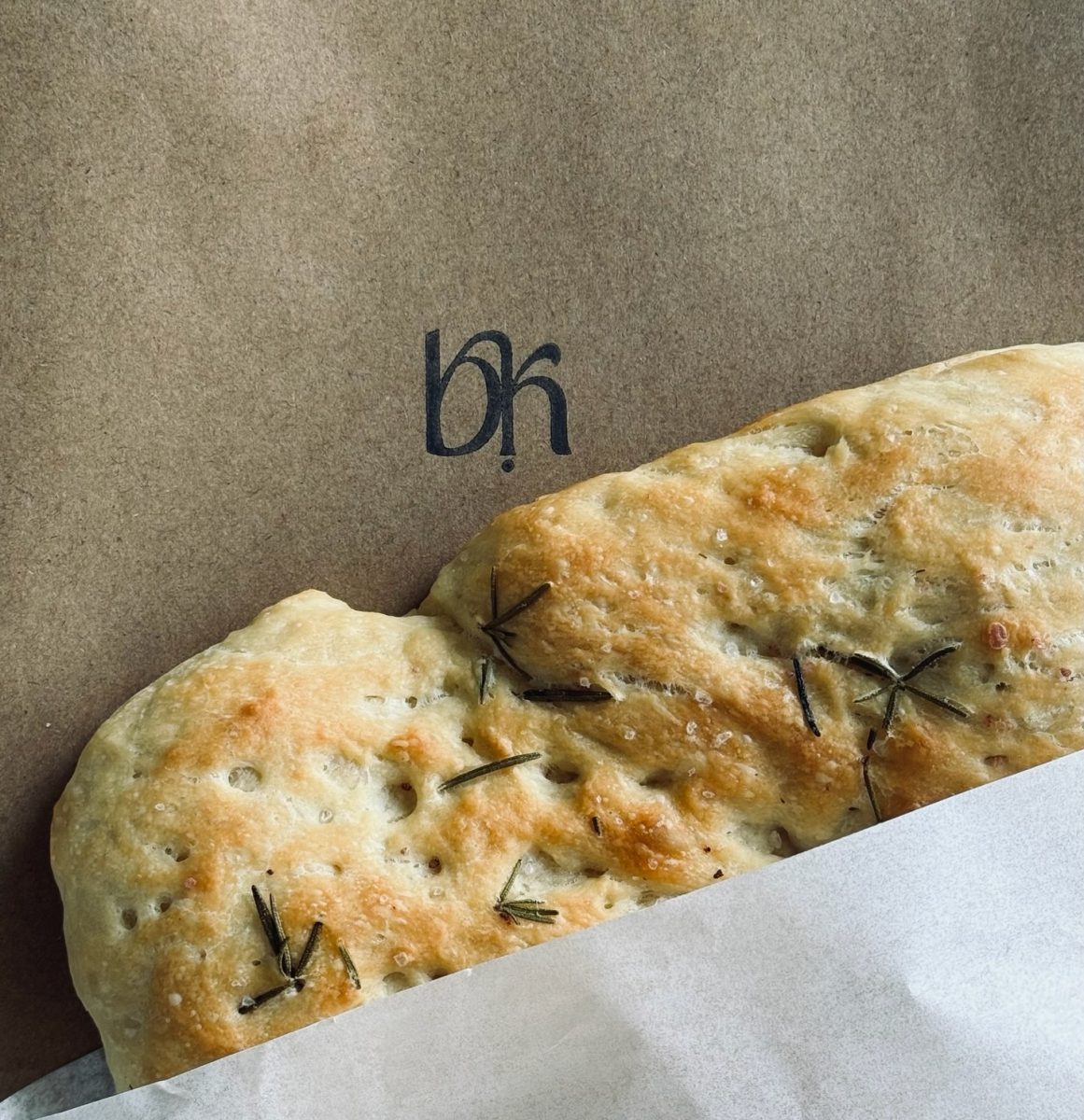 Focaccia with rosemary sitting on a brown paper bag with the Bink logo.