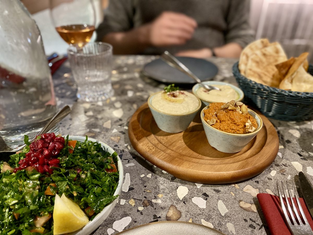 A restaurant table with three ramekins of different coloured dips, a plate of green salad and a basket of flatbread.