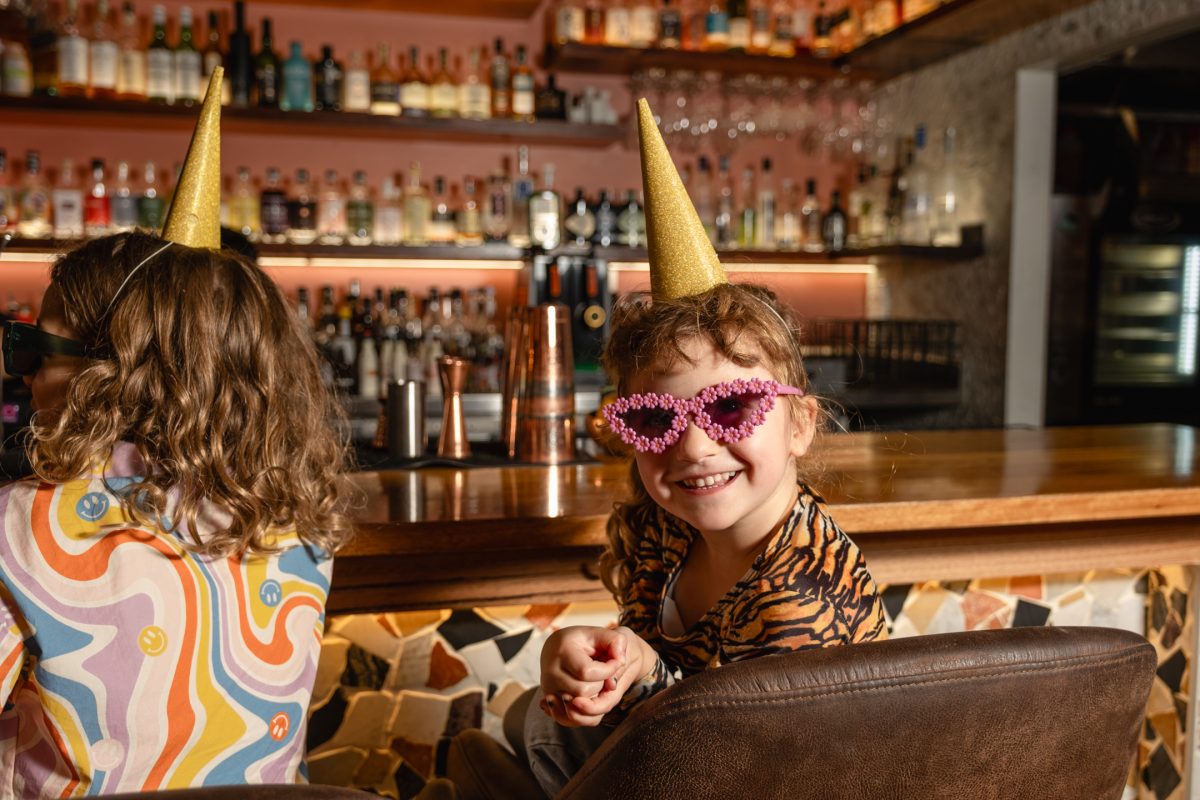 Two children sit at Bar Beirut dressed up with party hats and sunglasses.