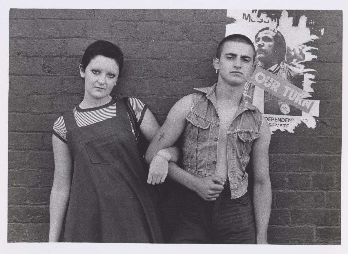 Male and female figures against a wall