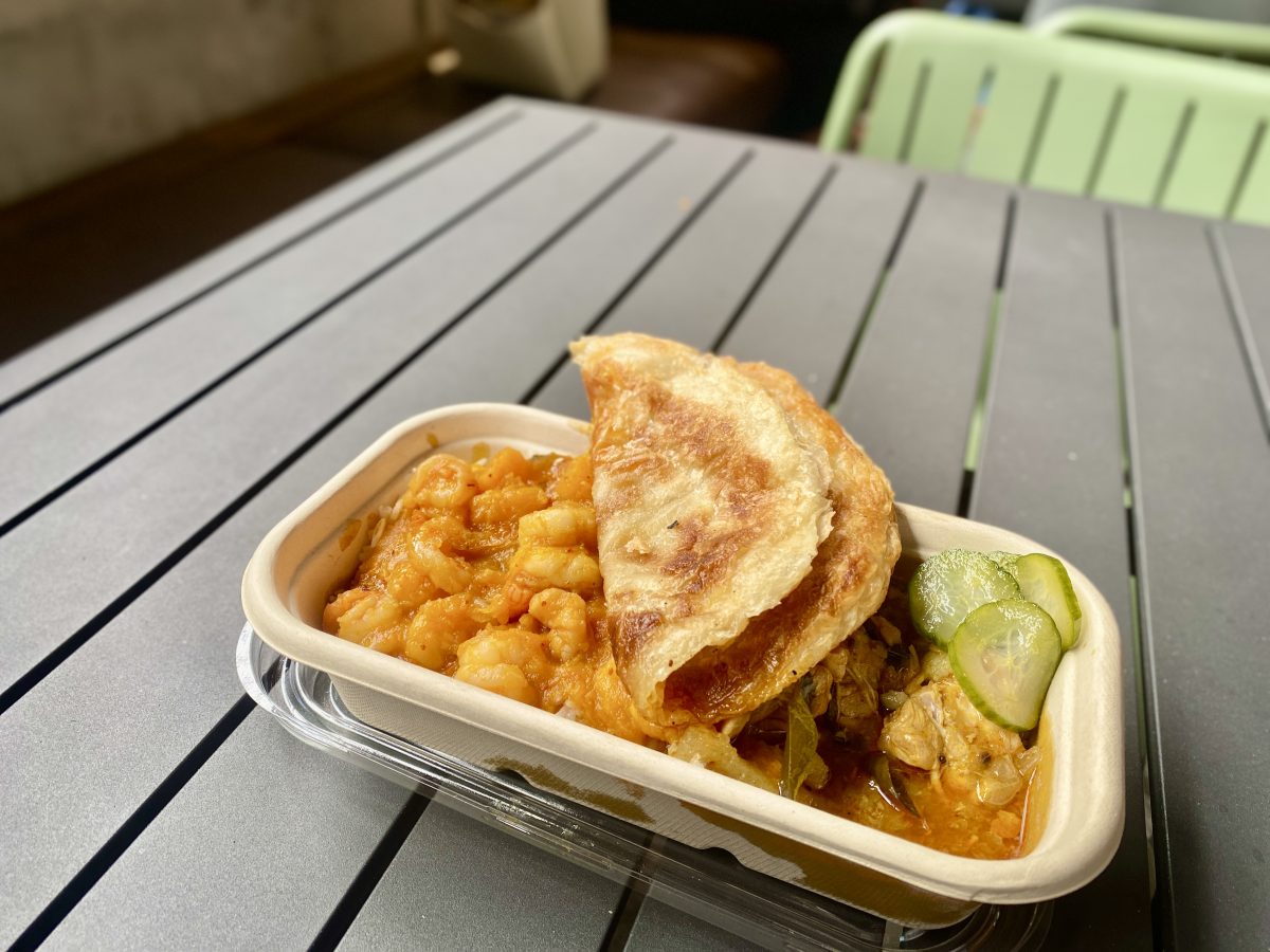 A takeaway box of curries with folded roti bread