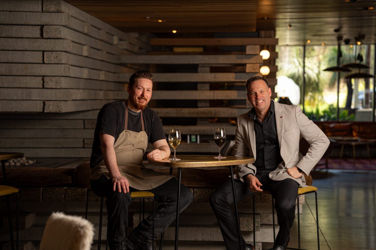 Two men sit at a table and smile for the camera.