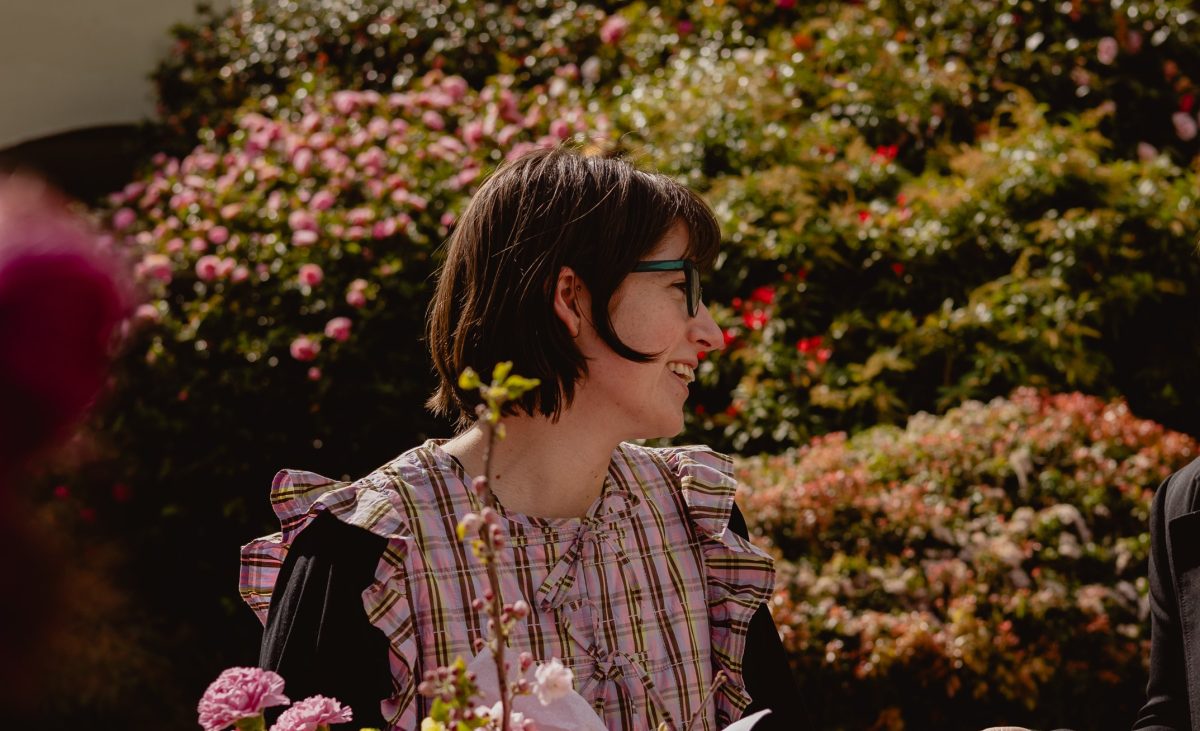 Caitlin wears a pink patterned shirt and sits in a garden.