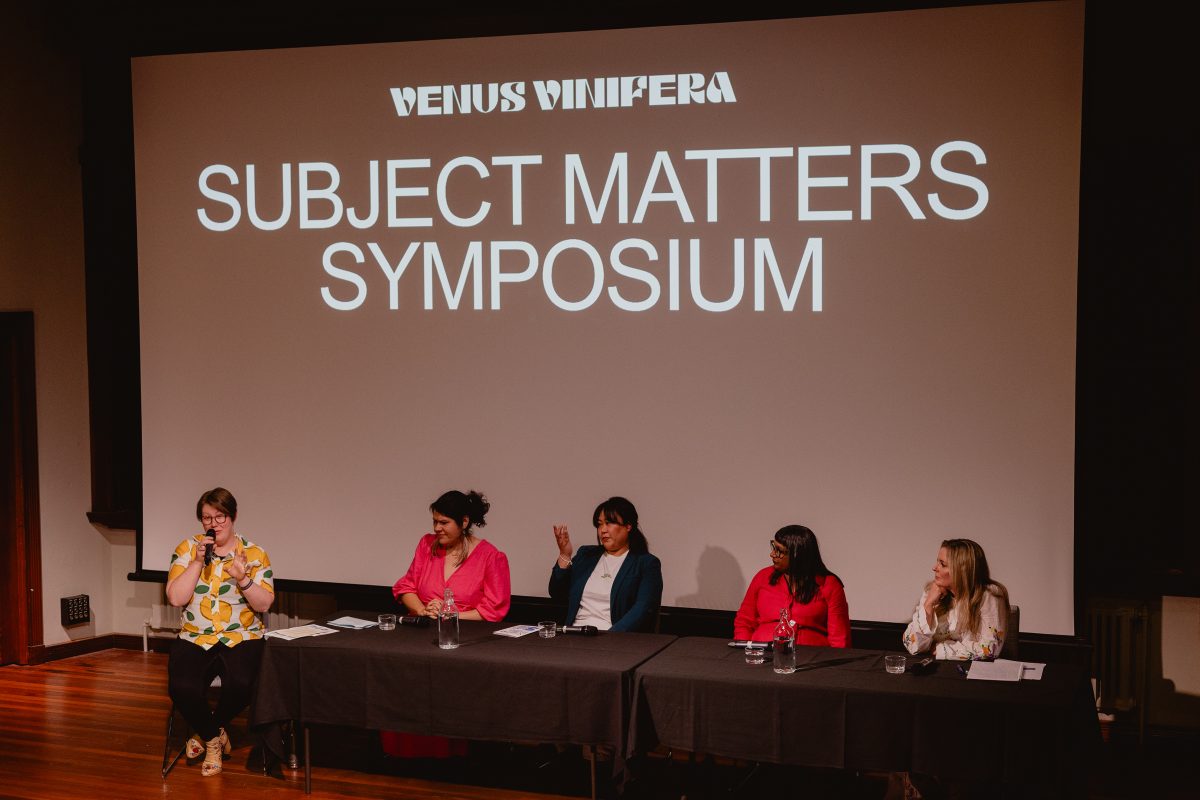 A panel of five women sit on a stage