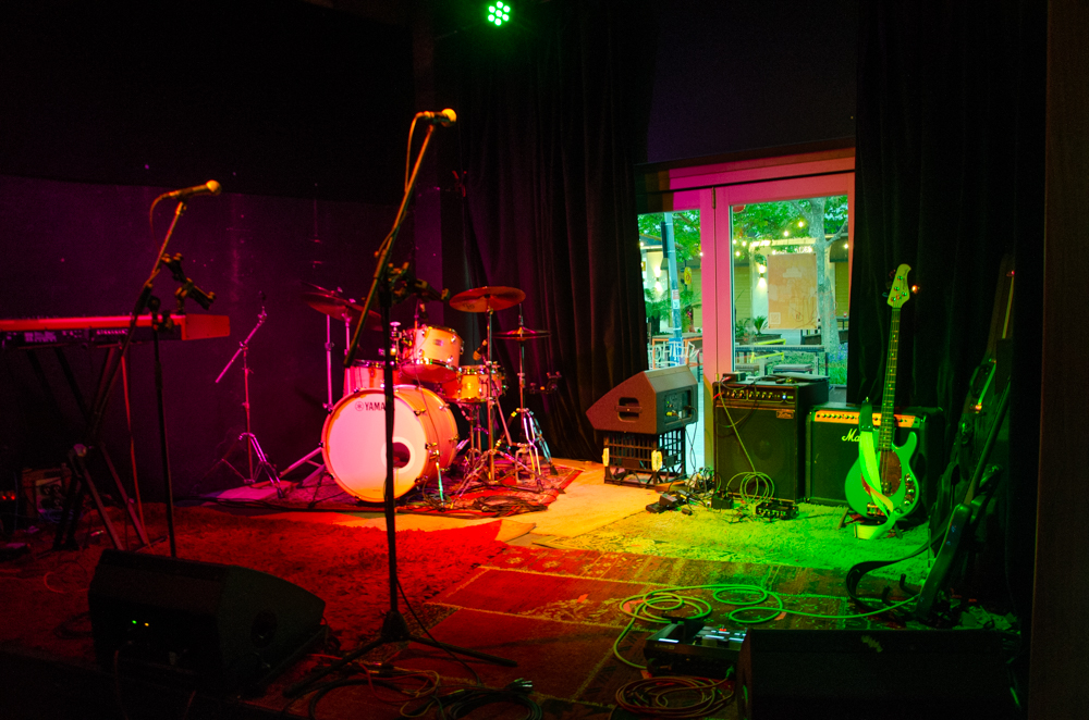 A stage with drumkit, amps and microphones is lit up in red and green.