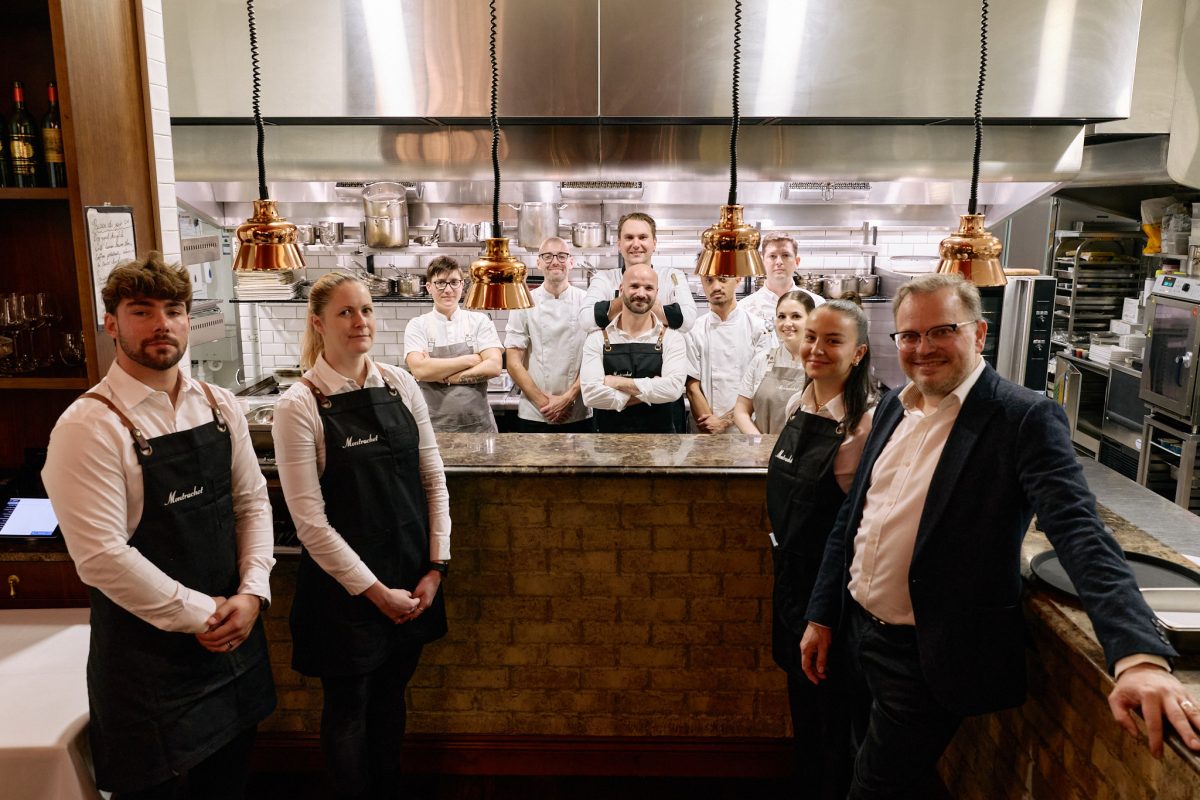 A group of staff in uniform pose for a photo at the kitchen pass of a restaurant.