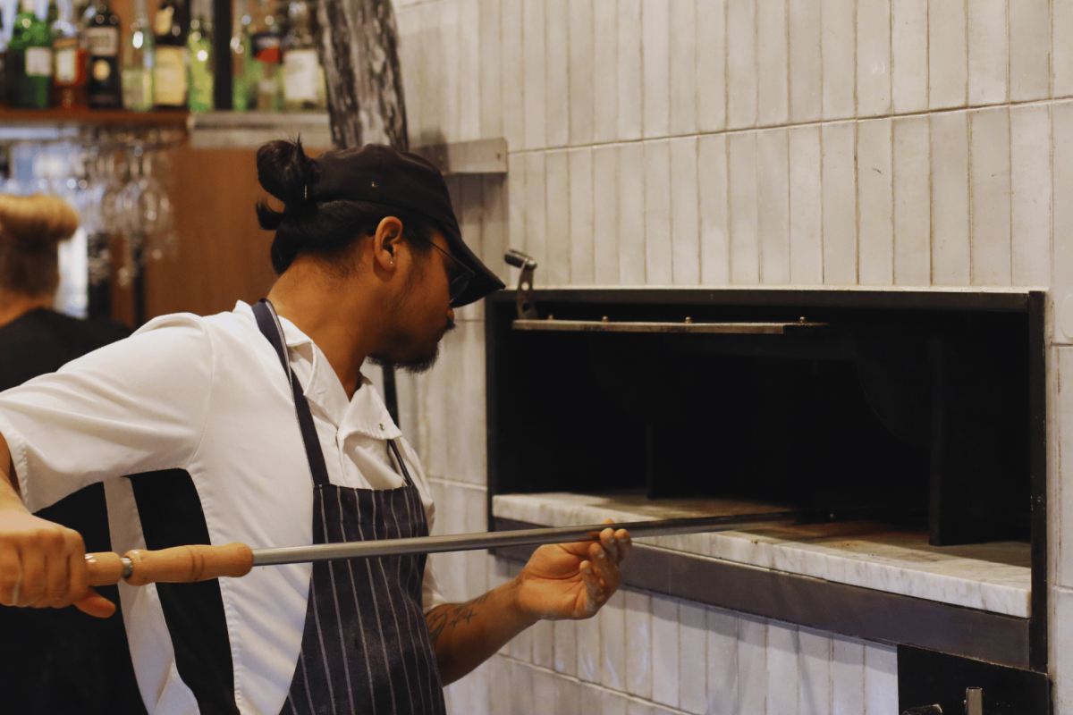 Pizza chef reaches into woodfired oven.