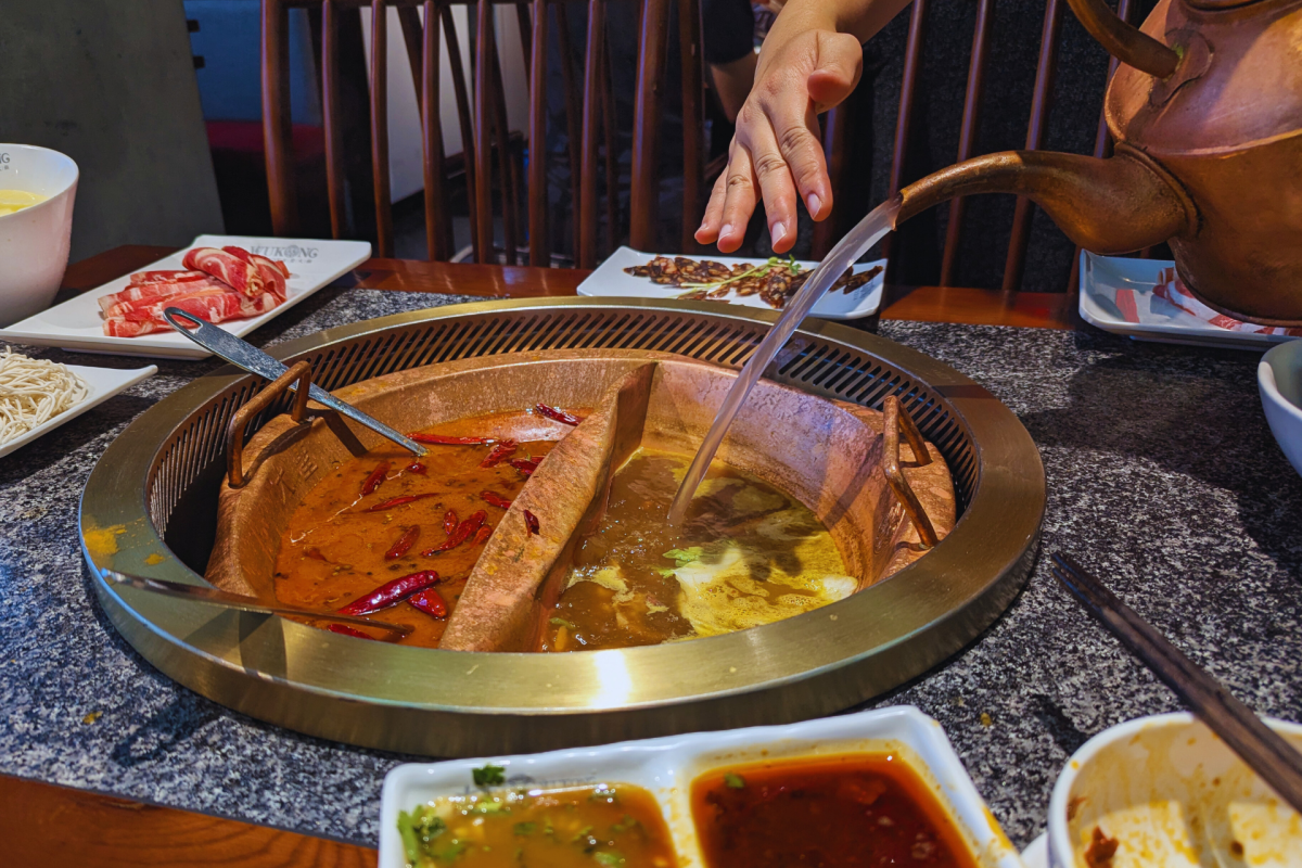 Boiling water being poured into a cauldron of broths.