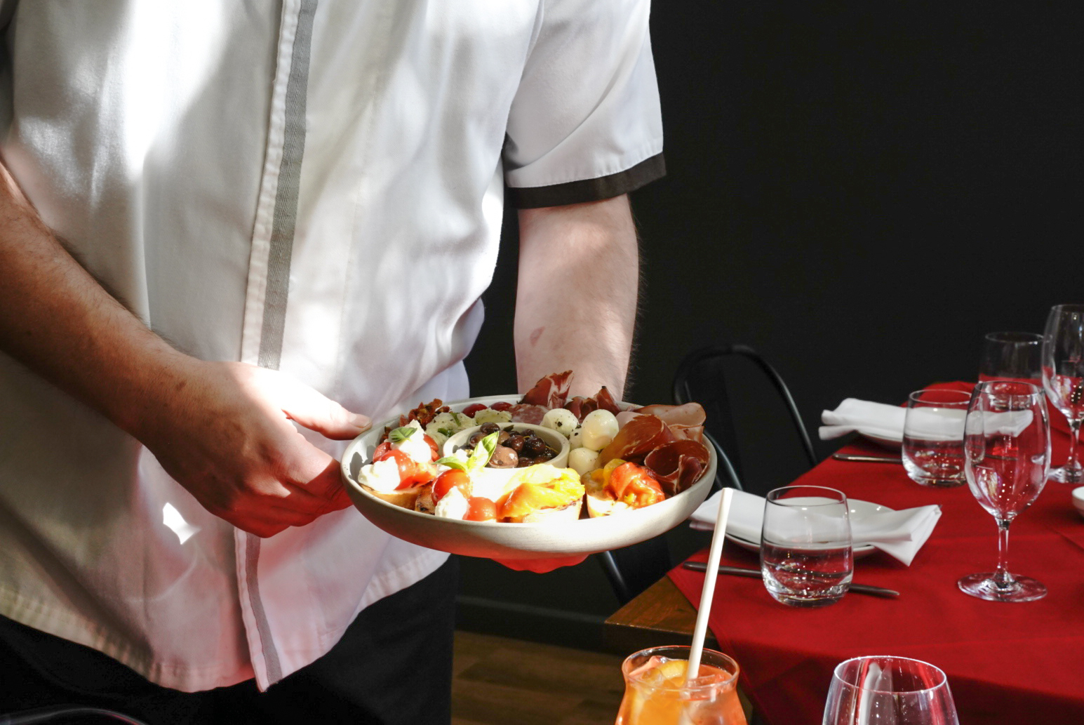 A chef holds a plate of antipasto in dappled sunlight.