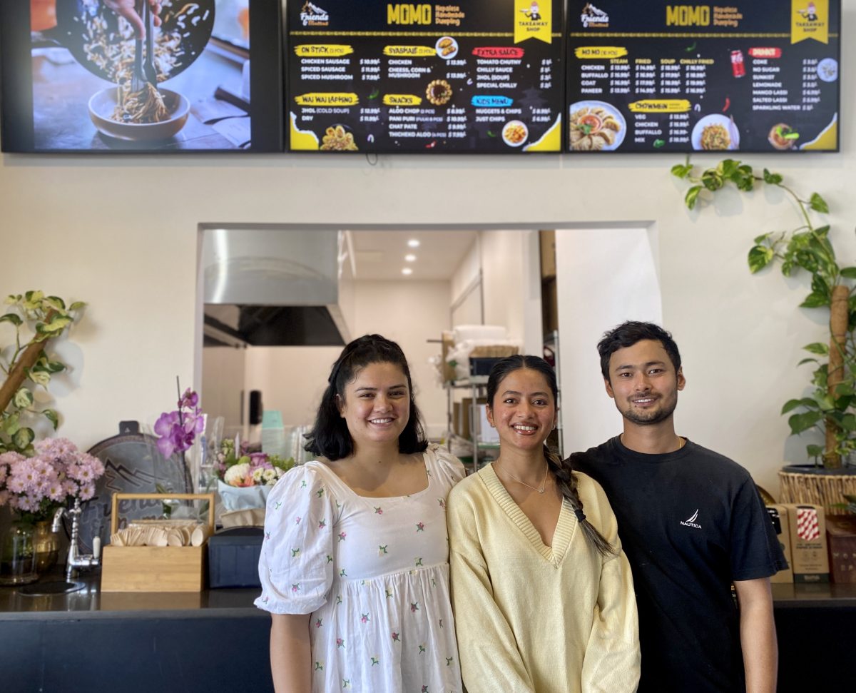 Three people stand under the menu sign at Friends and Momos.