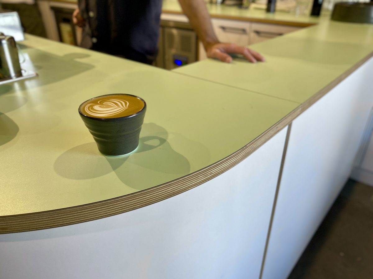 A beautiful cup of coffee in a handmade black mug sitting on a mint green benchtop. 