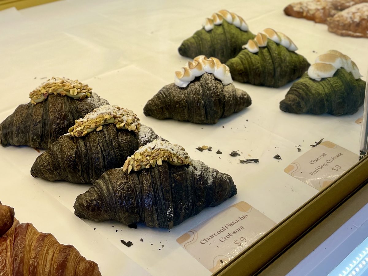 Charcoal crossaints topped with pistachios and other baked goods in a pastry cabinet.