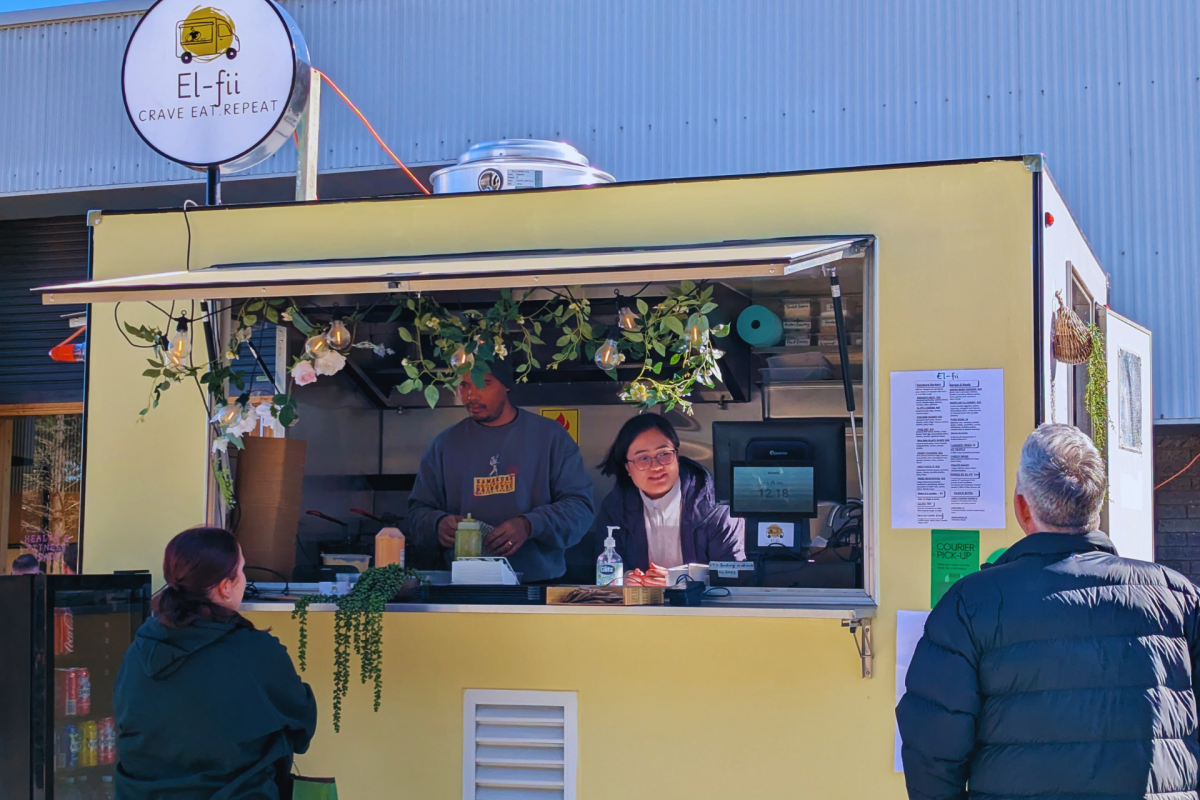 Two people serving in window of yellow food truck.