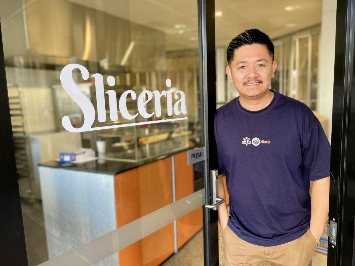 A man with moustache leans agains a glass door which reads Sliceria