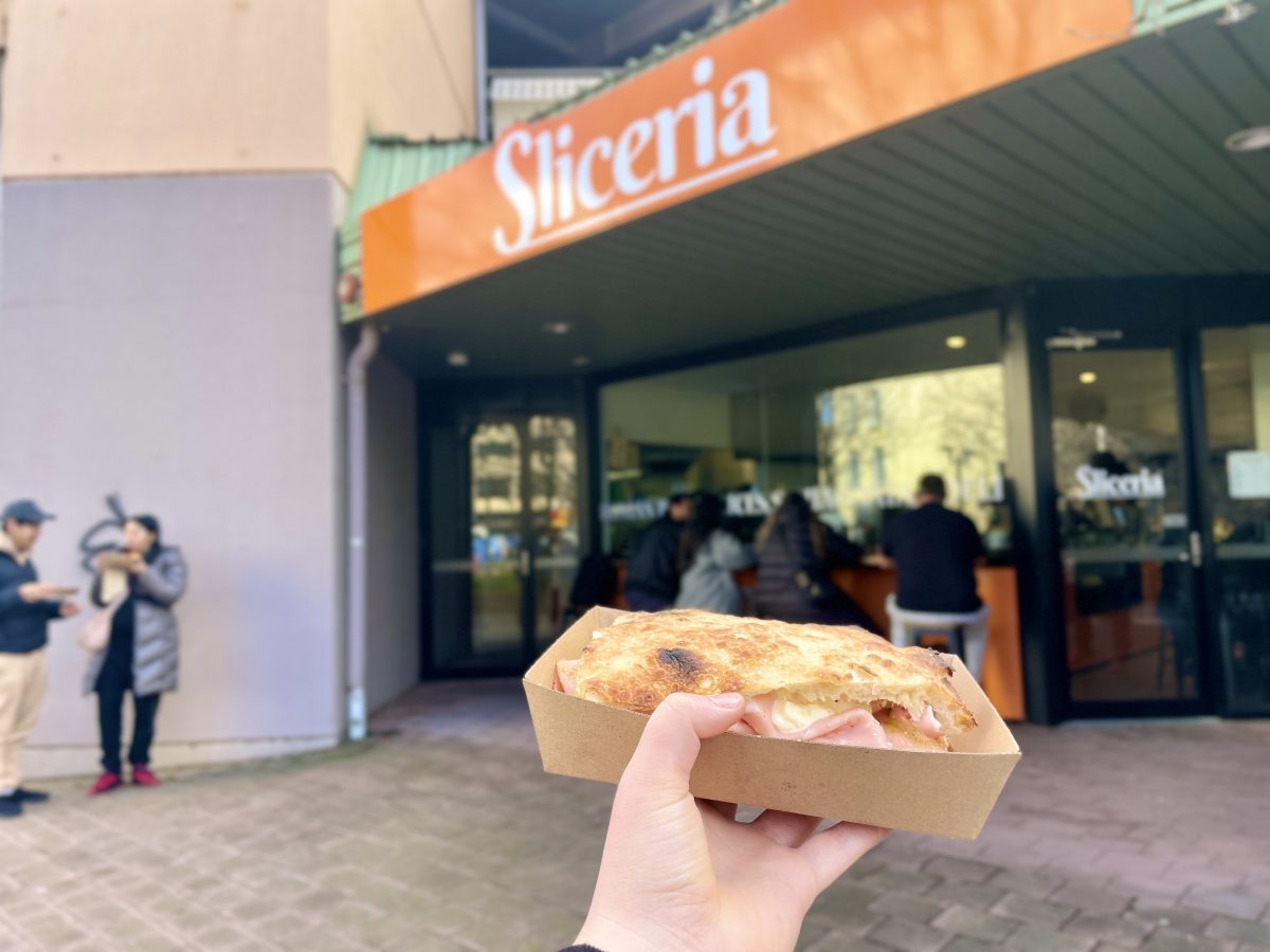 A hefty mortadella sandwich in takeaway box outside Sliceria