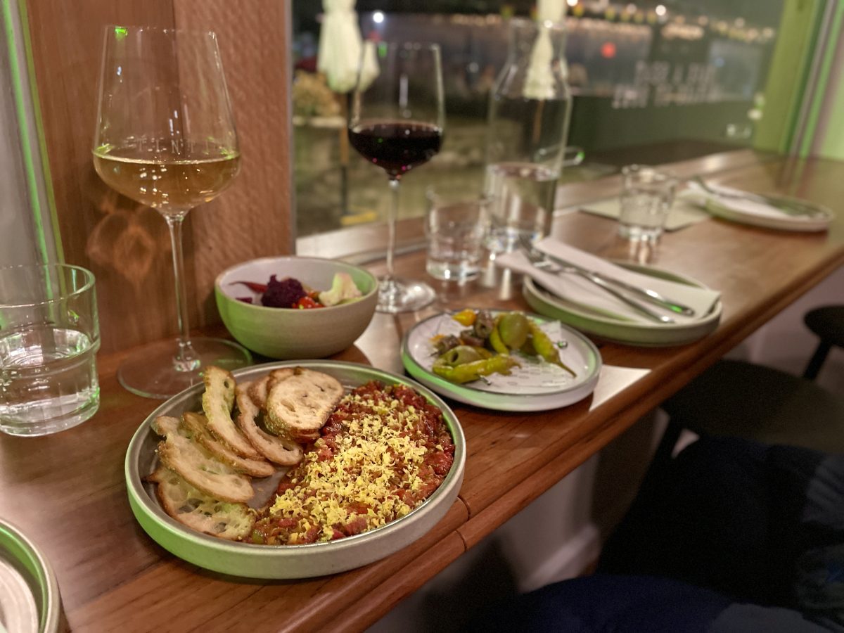 A window bench with glasses of wine and small plates of food.