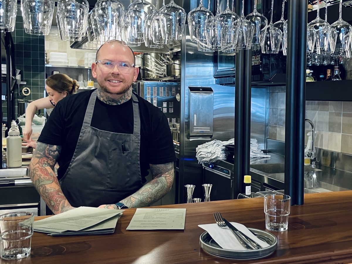 A tattooed chef stands behind the bar.