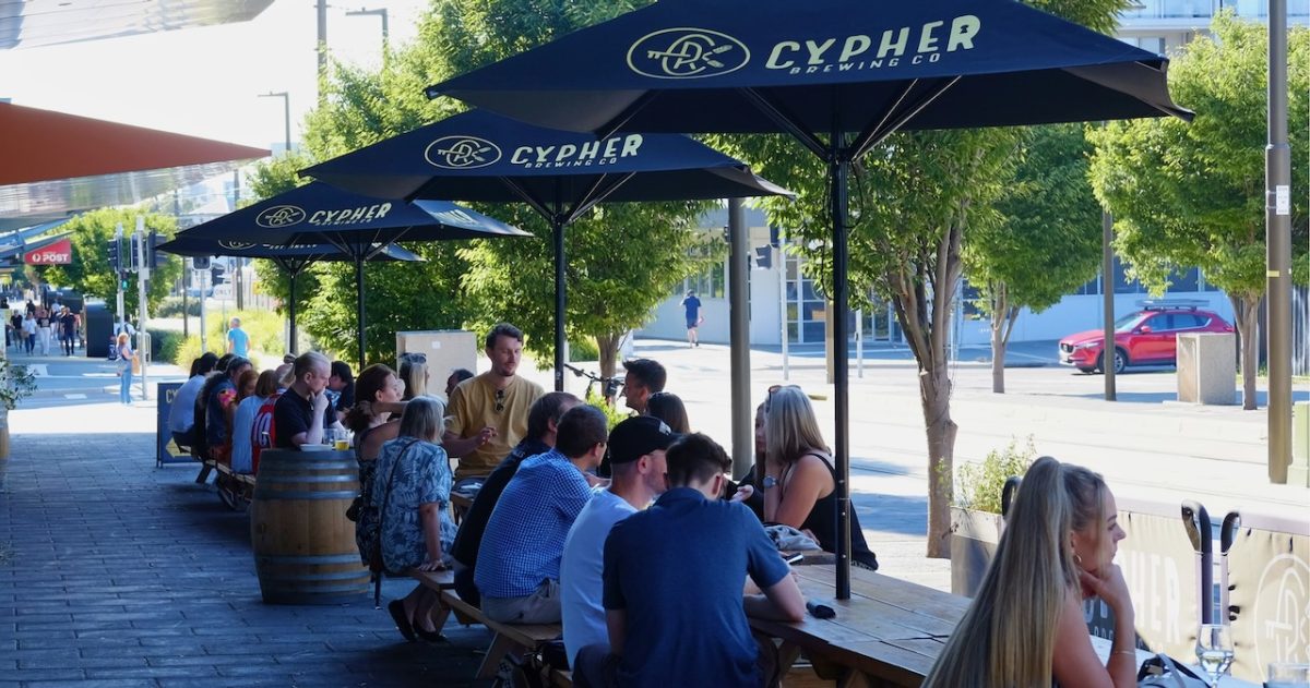 A group of people sit outside drinking beers under Cypher branded umbrellas.