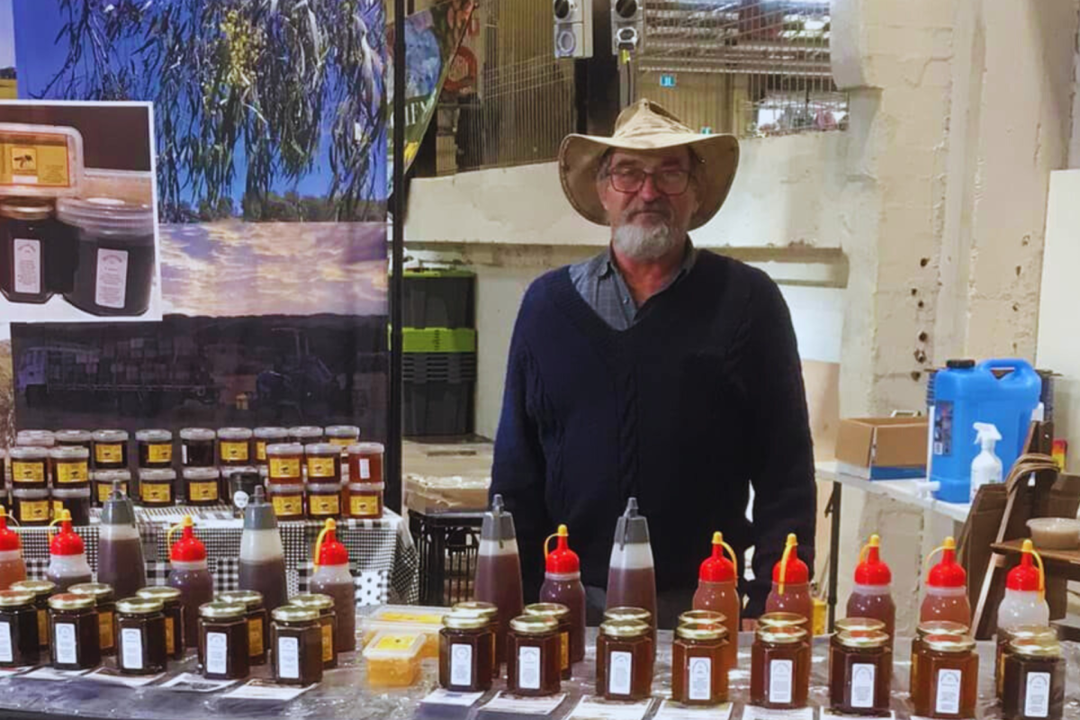Man standing at market stall selling honey.