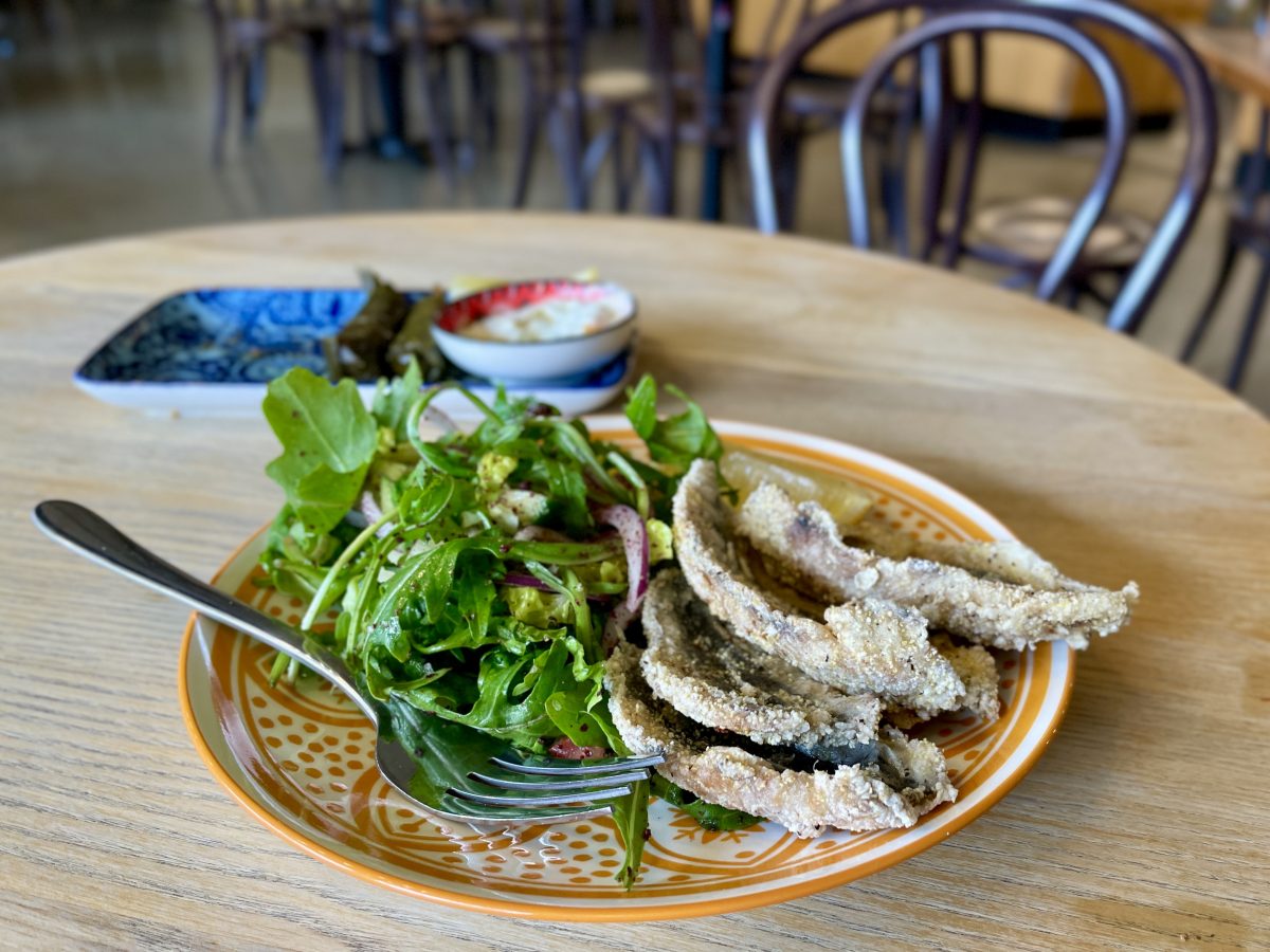 Fried sardines and a salad on a yellow patterned plate.