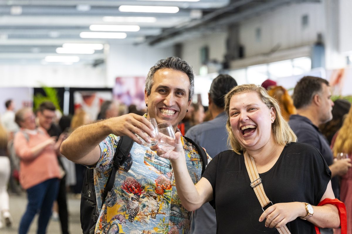 Two people 'cheers' their glasses and smile at the camera.