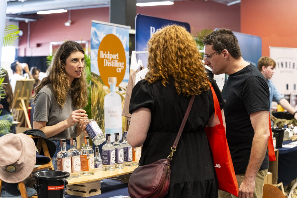 A woman shows a bottle to two people at a stall.