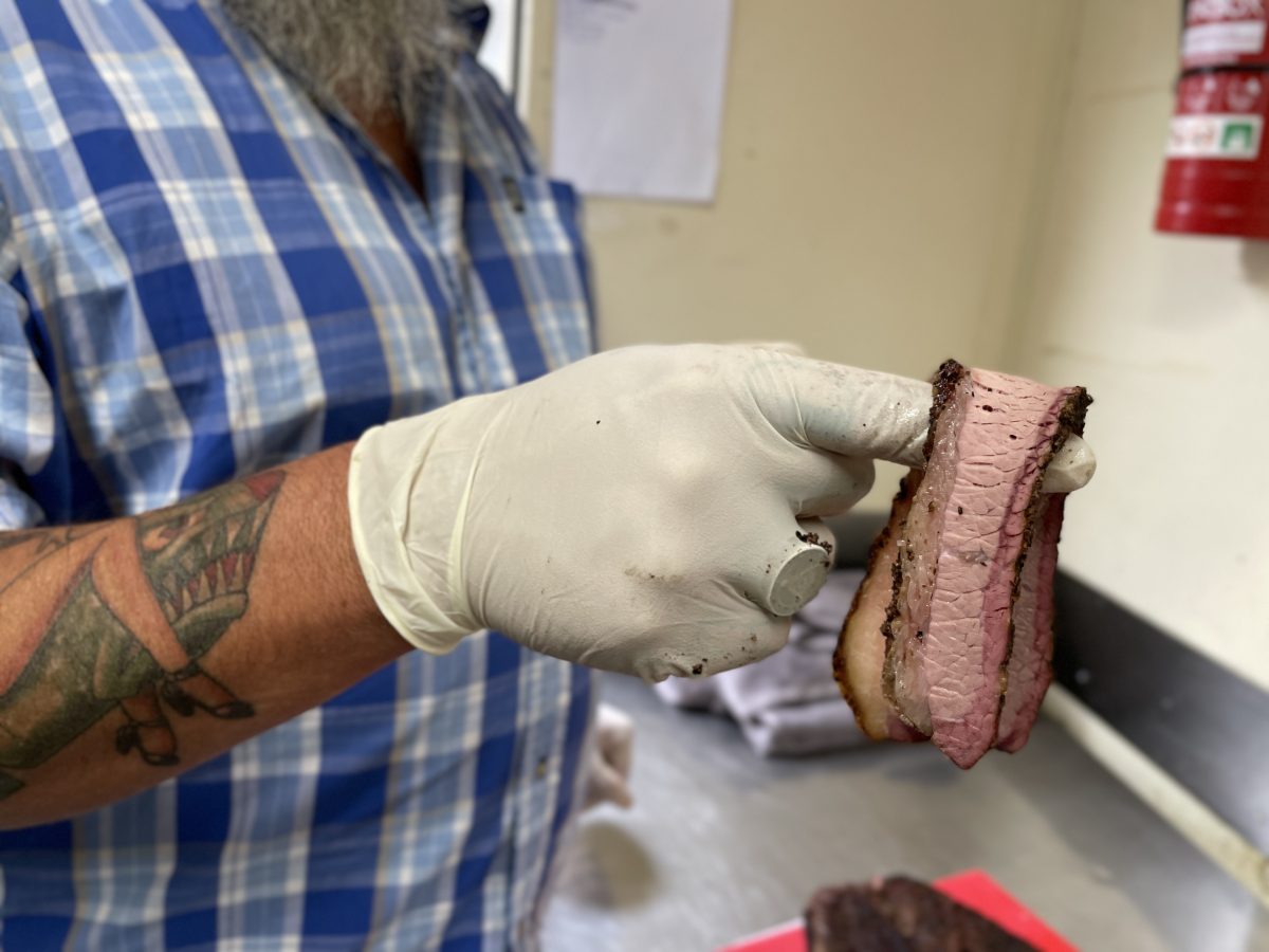 A gloved hand holds a juicy looking slice of brisket.