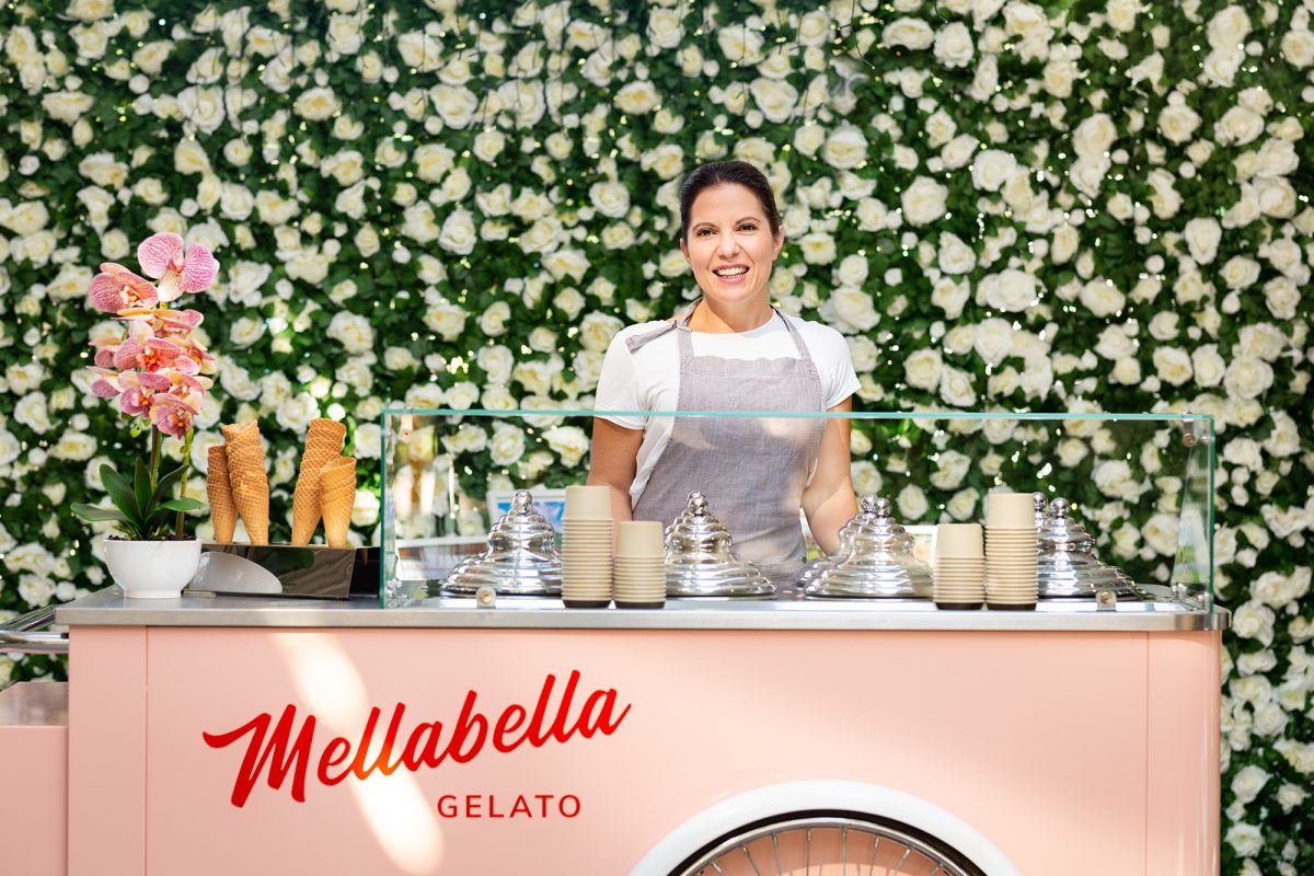 Melany wears a white t-shirt and grey apron, and stands behind a pink gelato cart.