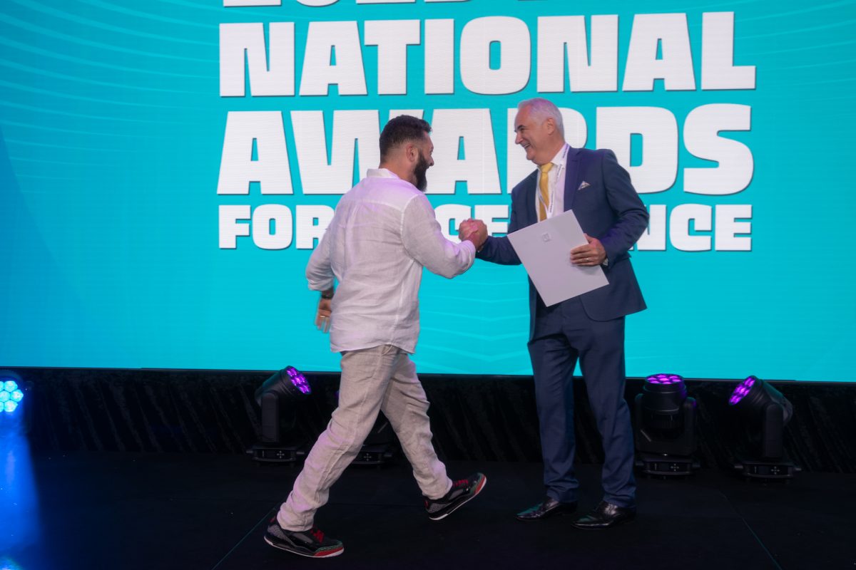 Man strides onto stage to accept award.