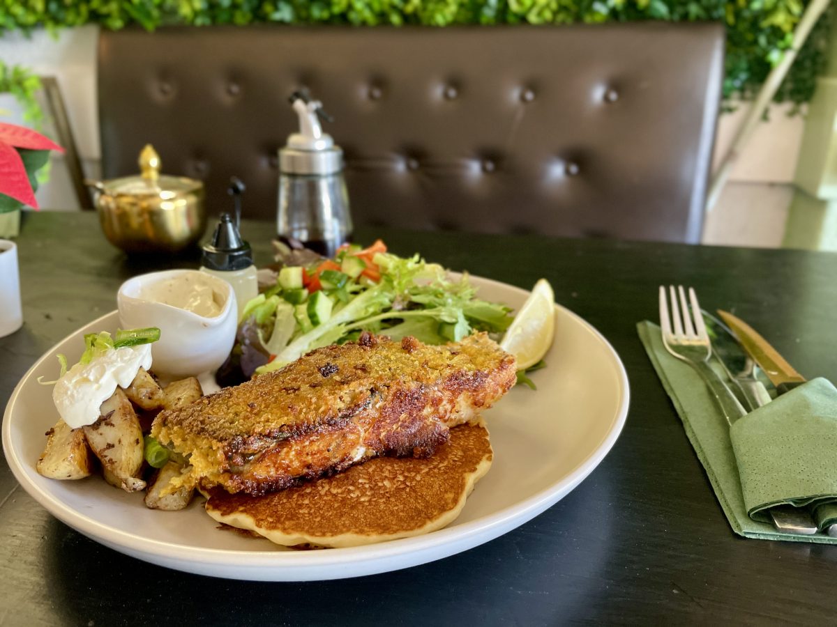 A piece of crumbed fish on a pancake with wedges and salad.