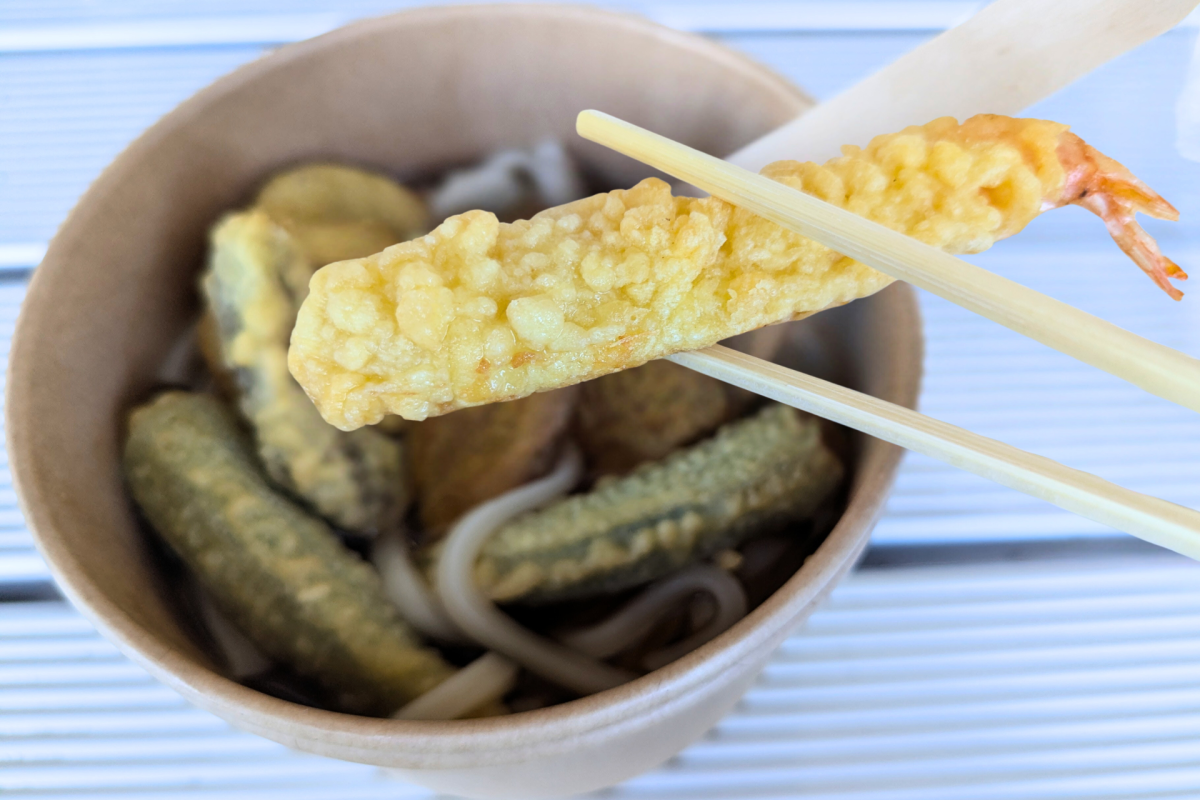 Battered prawn being held by chopsticks.