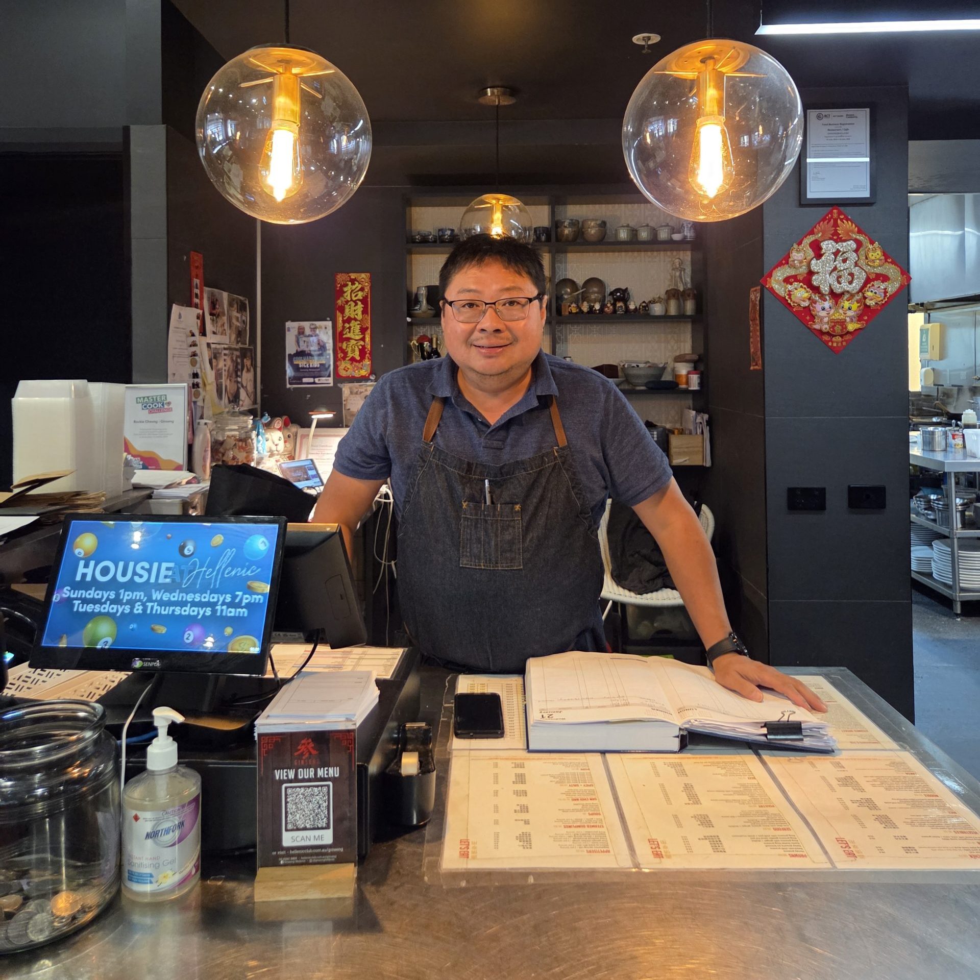 A man with glasses and an apron stands behind a restaurant counter. 