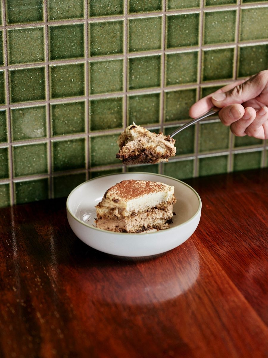 Bowl of tiramisu with a hand taking a spoonful.