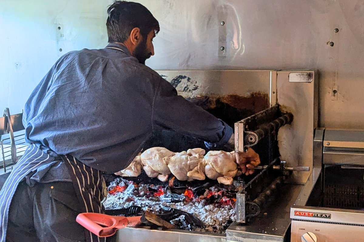 Man puts a spit of chickens over hot coals.